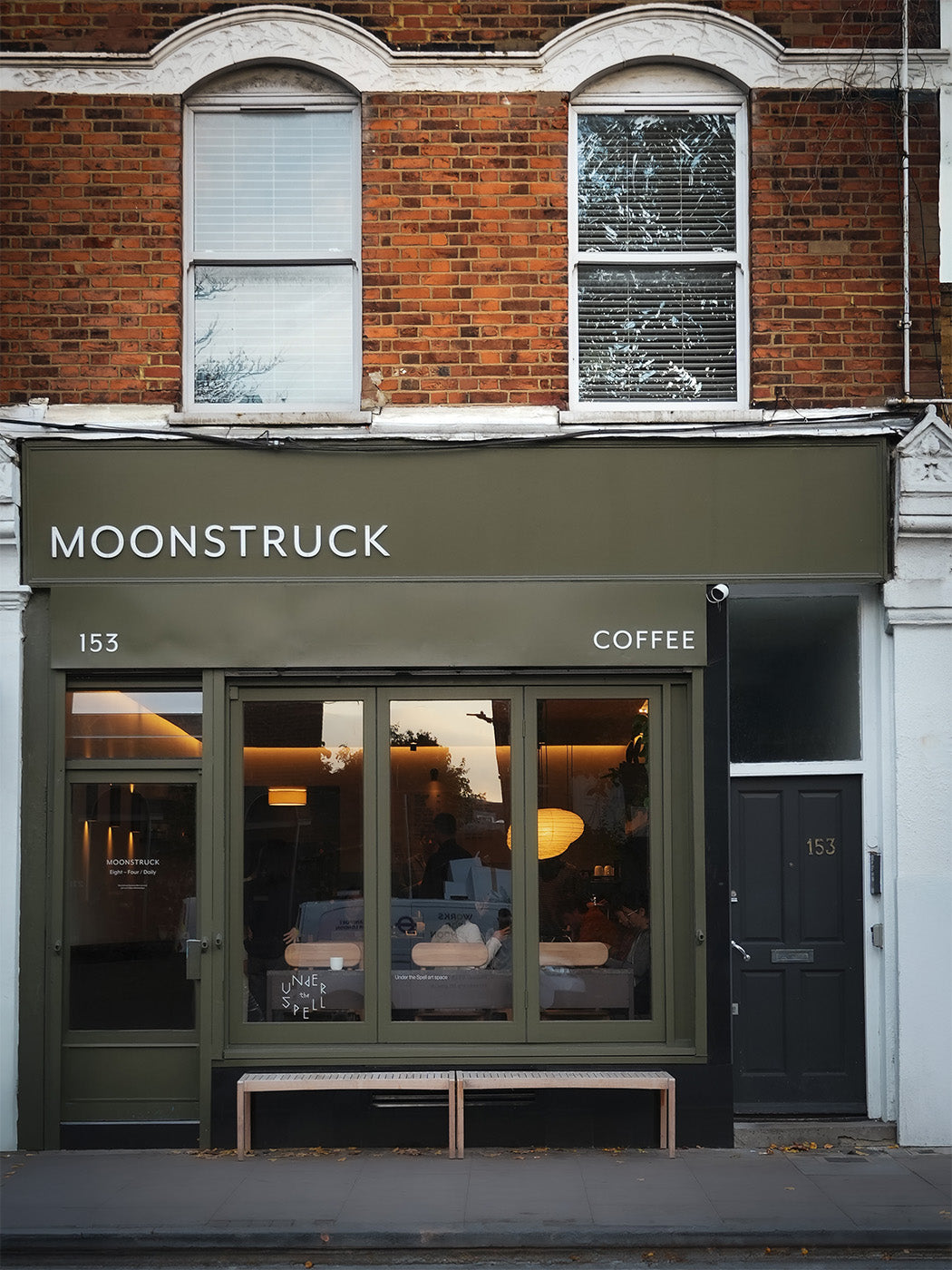 Front exterior of Moonstruck Coffee at 153, featuring an olive green awning and window frame, brick building facade above, and a dark door on the right.